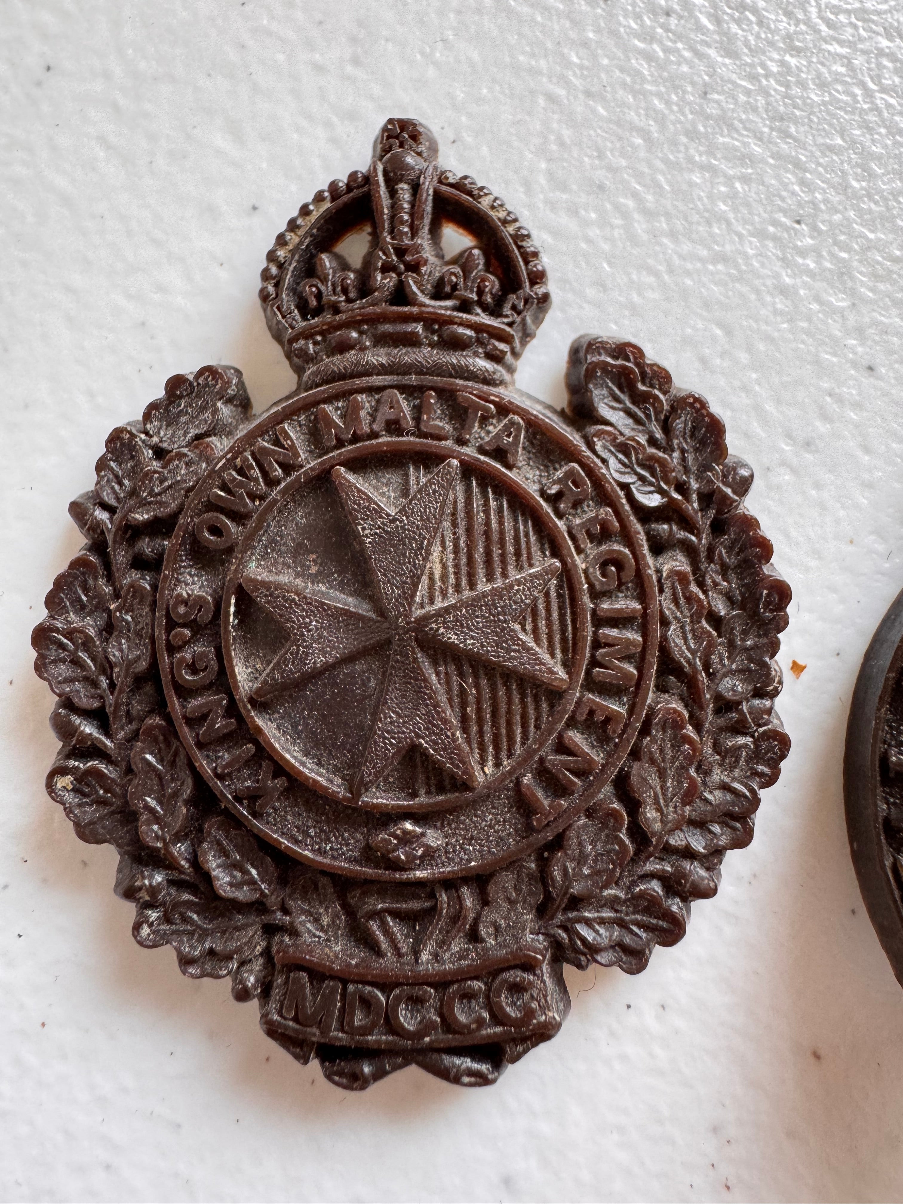 Lot 43: A rare Second World War period King's Own Malta Regiment economy plastic cap badge + other (Estimate £100-200)